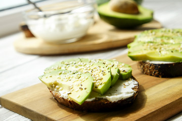 Vegan sandwich, rye bread toast, avocado, vegenaise eggless mayonnaise sauce, sesame seeds seasoning, white wood texture table. Vegetarian nutrition. National avocado day concept. Close up, background