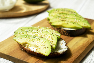 Vegan sandwich, rye bread toast, avocado, vegenaise eggless mayonnaise sauce, sesame seeds seasoning, white wood texture table. Vegetarian nutrition. National avocado day concept. Close up, background