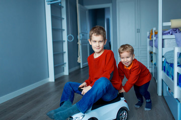 Fototapeta na wymiar Two happy children riding on baby car in room, indoors.