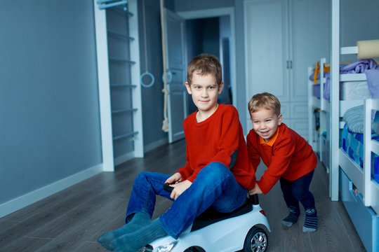 Two happy children riding on baby car in room, indoors.