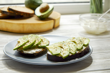Vegan sandwich, rye bread toast, avocado slices, vegenaise sauce & raw arugula. Toasted sourdough, eggless mayonnaise, wooden table, whole & halved. National avocado day concept. Close up, background.