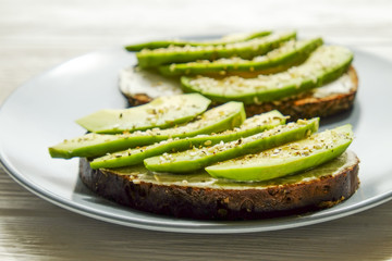 Vegan sandwich, rye bread toast, avocado, vegenaise eggless mayonnaise sauce, sesame seeds seasoning, white wood texture table. Vegetarian nutrition. National avocado day concept. Close up, background