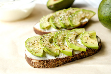 Vegan sandwich, rye bread toast, avocado, vegenaise eggless mayonnaise sauce, sesame seeds seasoning, white wood texture table. Vegetarian nutrition. National avocado day concept. Close up, background