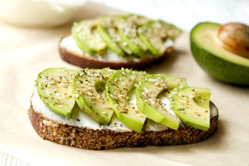 Vegan sandwich, rye bread toast, avocado, vegenaise eggless mayonnaise sauce, sesame seeds seasoning, white wood texture table. Vegetarian nutrition. National avocado day concept. Close up, background