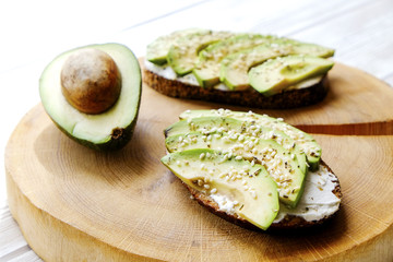Vegan sandwich, rye bread toast, avocado, vegenaise eggless mayonnaise sauce, sesame seeds seasoning, white wood texture table. Vegetarian nutrition. National avocado day concept. Close up, background