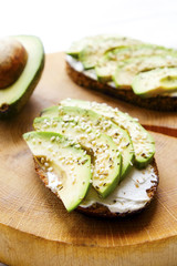 Vegan sandwich, rye bread toast, avocado, vegenaise eggless mayonnaise sauce, sesame seeds seasoning, white wood texture table. Vegetarian nutrition. National avocado day concept. Close up, background