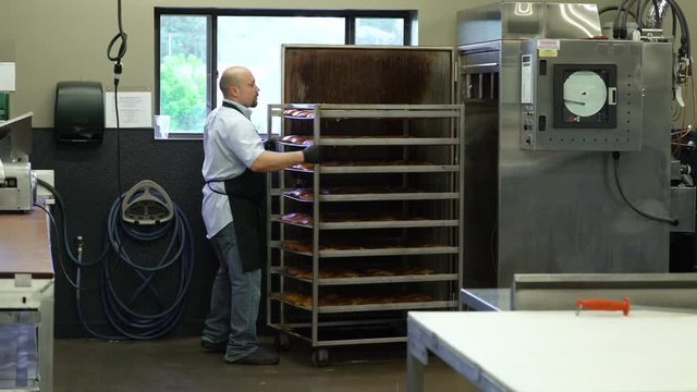 Butcher pulling racks of fish out of a commercial smoker
