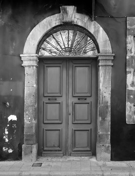 monochrome image of old back doors in an arched stone frame with flaking painted walls
