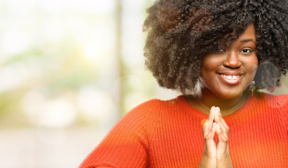 Beautiful african woman with hands together in praying gesture, expressing hope and please concept,...