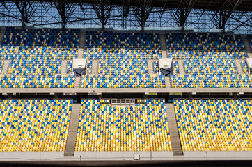 Naklejka premium Niewyraźne siedzi fanów kolorowe plastikowe krzesła na tle stadionu piłkarskiego. Puste boisko piłkarskie stadionu zielona trawa na arenie lekkoatletycznej piłki nożnej.