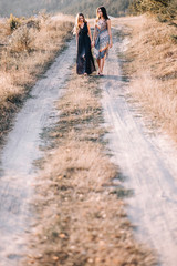 Obraz premium beautiful young girls walking in the light of long summer dresses for mountainous terrain, sand and posing. the wind and the sunset