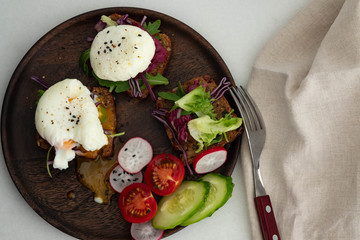 Top view of healthy breakfast with poached egg on rye bread on a wooden table.
