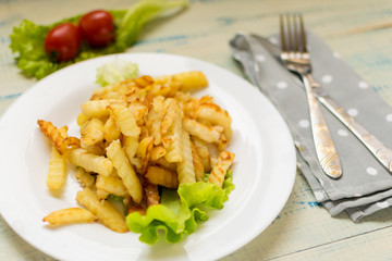 French fries with meat on a white plate on a wooden light background.