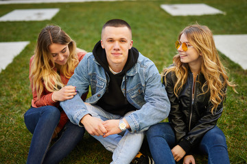 Naklejka premium Boy with two girls on the green grass talking and smile to camera