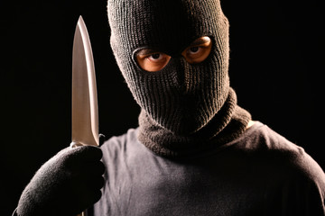 The robber hold the knife in hand on black background