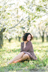 gardening, arrangement, weekends concept. in the middle of the forest in bloom full of fresh foliage and flowers of dendelions there is a wonderful woman who is sitting on the ground