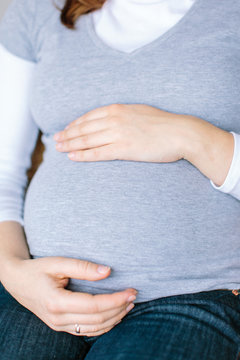 motherhood, family, pregnancy concept. close up of hands of young pregnant lady with golden engagement ring, she is hugging her belly with baby on it