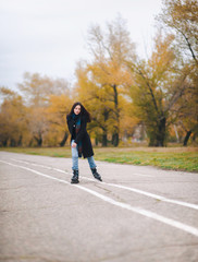 A pretty young girl in a coat and with a long scarf happily skates in the autumn park. Fighting the autumn depression. To overcome depression.