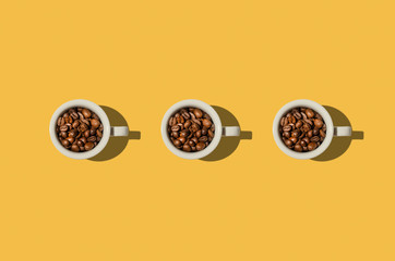 Cup concept. White cups with coffee beans on yellow background.  Creative style.