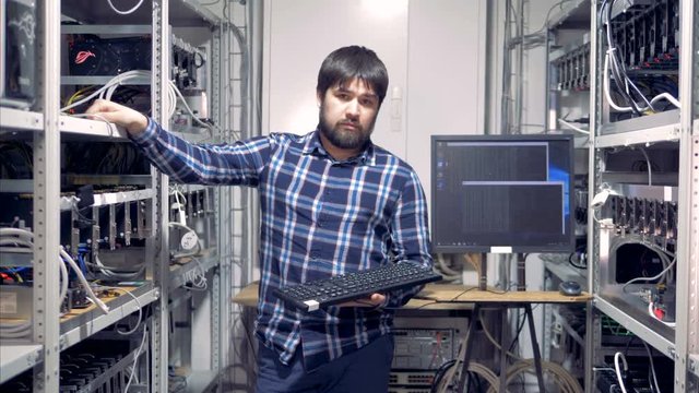 Cryptocurrency mining specialist is standing in a mining rig unit and looking into the camera