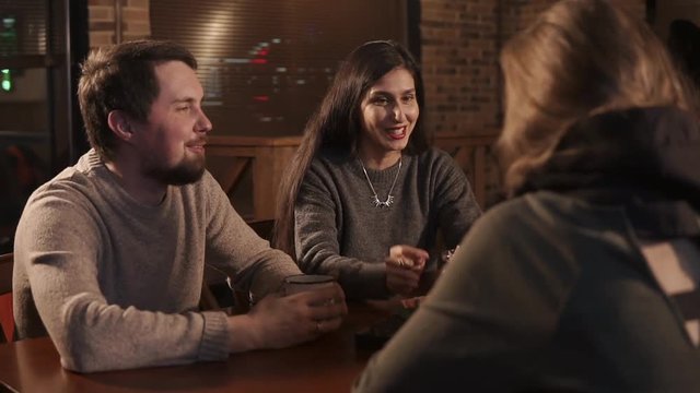 Cheerful girl is talking with her friends in a pub. Group of young people are having fun and resting in weekends and drinking
