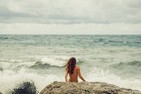 540px x 360px - Naked young girl with a beautiful body stands facing the sea, back to the  beach and watching the raging, mighty, strong waves during a storm in the  ocean. Beach and stones. Stock