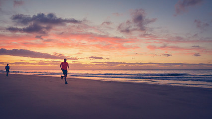 Fototapeta na wymiar Two runners are running on the beach at sunrise.