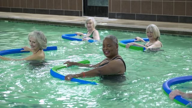 Mature adults exercising with pool noodles in swimming pool.