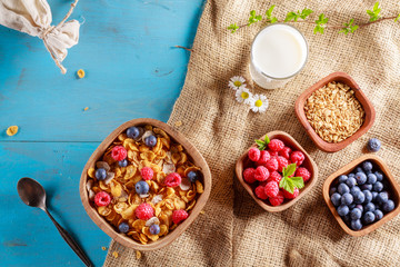 Cornflakes and other cereals with fresh fruits of raspberries, blueberries and milk on healthy breakfast. Above view.