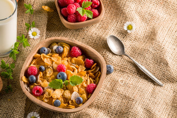 Cornflakes and other cereals with fresh fruits of raspberries, blueberries and milk on healthy breakfast.