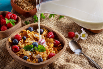 Cornflakes and other cereals with fresh fruits of raspberries, blueberries and pouring milk on healthy breakfast.