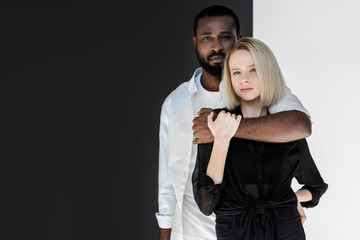african american boyfriend hugging attractive blonde girlfriend near black and white wall