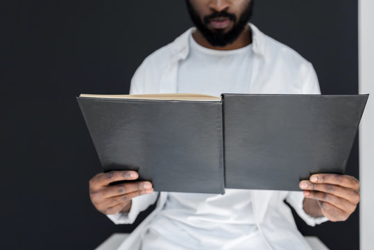 cropped image of stylish african american man in white clothes reading black book