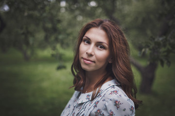 Beautiful smiling young brunette woman in a green summer garden amid the Apple trees with green fruit.