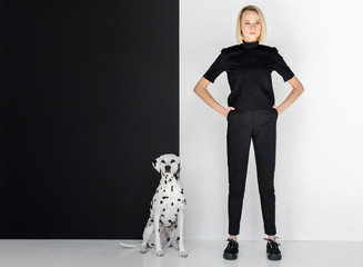 beautiful stylish blonde woman in black clothes standing near black and white wall with dalmatian...