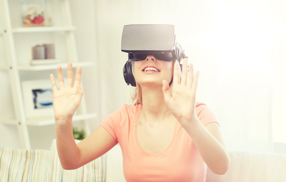 technology, virtual reality, entertainment and people concept - happy young woman in virtual reality headset or 3d glasses and headphones playing game at home and touching something invisible