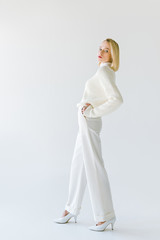 Fototapeta na wymiar side view of beautiful stylish blonde woman in white clothes posing on white