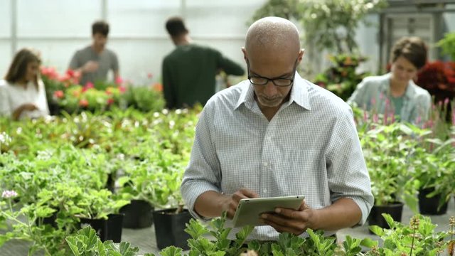 Man using digital tablet in garden centre, looking at camera, smiling.