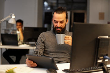 deadline, technology and people concept - creative man with tablet pc computer working late at night office and drinking coffee