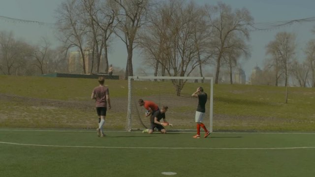 Football striker picking up soccer ball from goal's net and giving high five to teammate while celebrating a goal during football training match. Joyful team celebrating scoring a goal in the pitch.