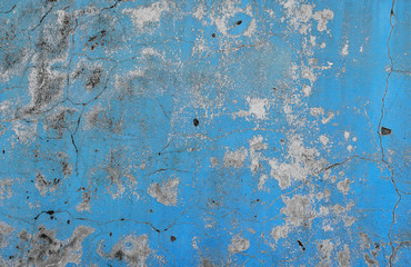 Texture of a concrete wall with a worn blue paint, damaged paint with some holes and cracks.