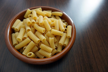 macarrones crudos, dentro de cuenco de barro,  perejil, fondo de madera