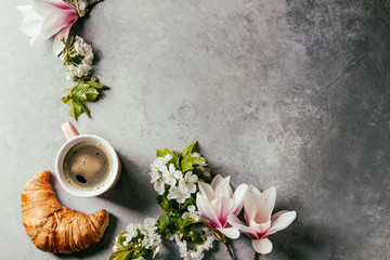 Pink mug of black espresso coffee, french croissant, cream and spring flowers magnolia, blooming...
