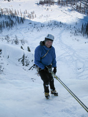 male ice climber smiling at the top of a hard icefall before getting ready to rappel to the bottom