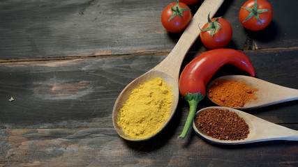 Red chili pepper, cherry tomatoes, turmelic, paprika and pepper flakes on black barn wood background.