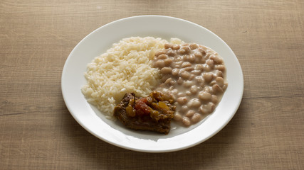 White rice, pinto beans and meat with sauce. White dish on wooden table.