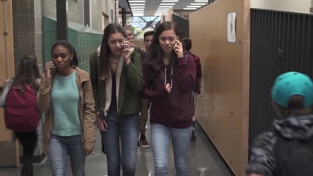 Medium shot of three friends talking on phone in school corridor
