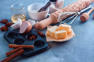 Cooking concept with baking tools and ingredients. A rolling pin, honey spoons, a muffin tin, a whisk, flour, buter and egg shell on a concrete background with copy space.