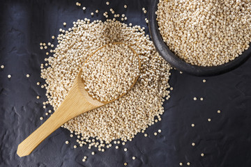 Quinoa grains with spoon and bowl on black background