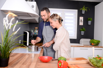 happy and cheerful young couple cooking organic vegetables together at home